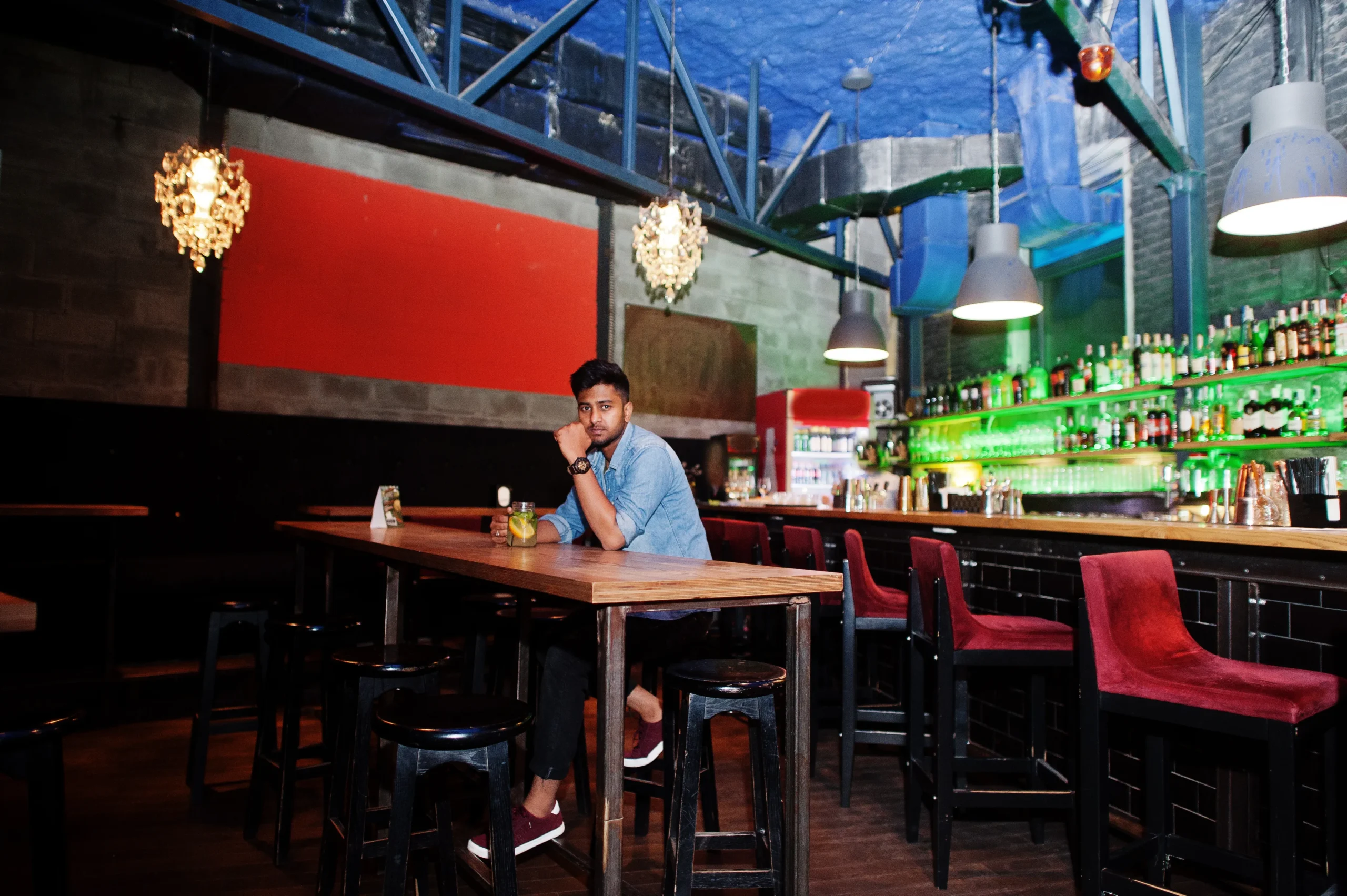 portrait-handsome-successful-bearded-south-asian-young-indian-freelancer-blue-jeans-shirt-sitting-night-club-against-bar-counter-with-cocktail-having-rest
